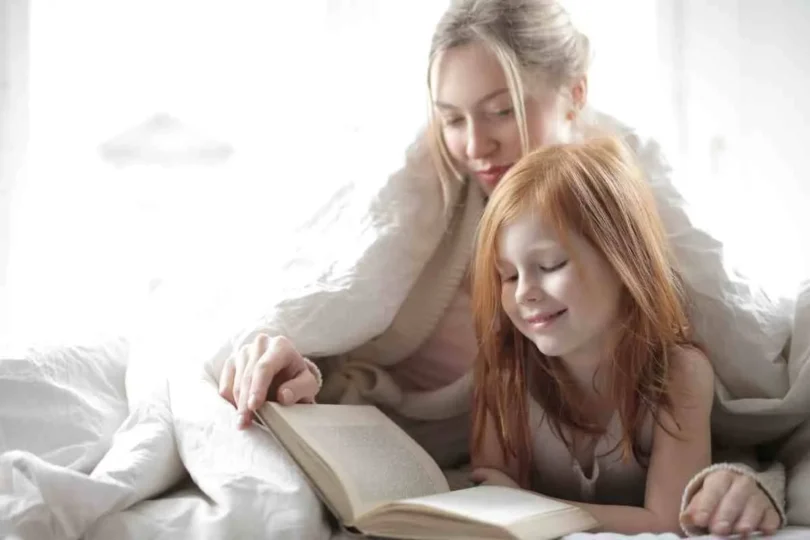 Fillette qui lit sous la couette avec sa mère.